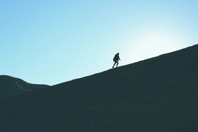 a lone person walking up a hill on a bright day