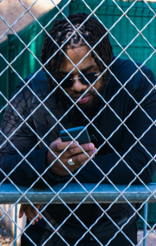 man in black jacket sitting on a fence and looking at cell phone