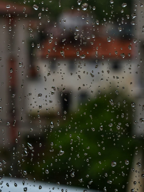 the window with rain is looking out over some buildings