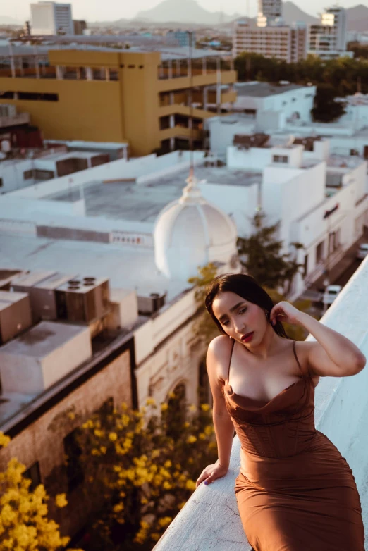 a woman in brown dress standing on balcony with city view