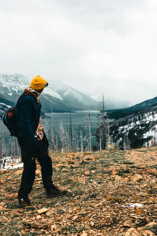 a person in yellow beanie standing next to a snow covered mountain