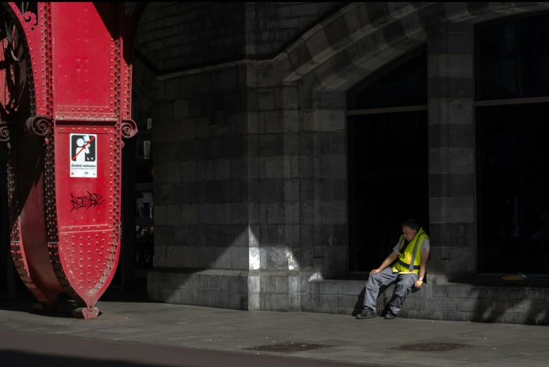 man sitting down on bench near red fire hydrant