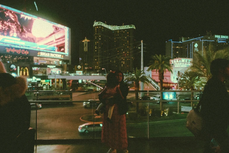 a woman stands on the balcony of a el and watches the neon city lights