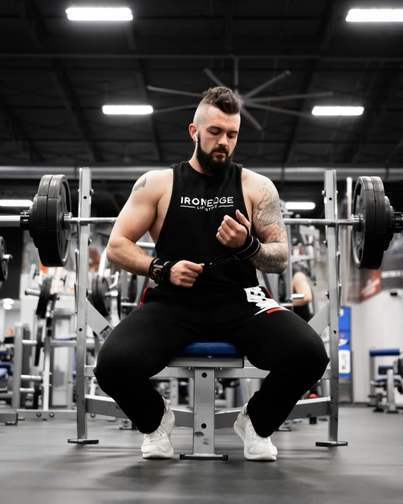 a man squats down in the gym, his hands are resting on a barbell