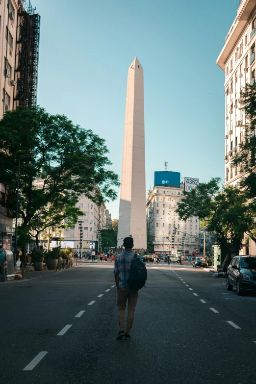 a lone man walking down the street near a tall monument