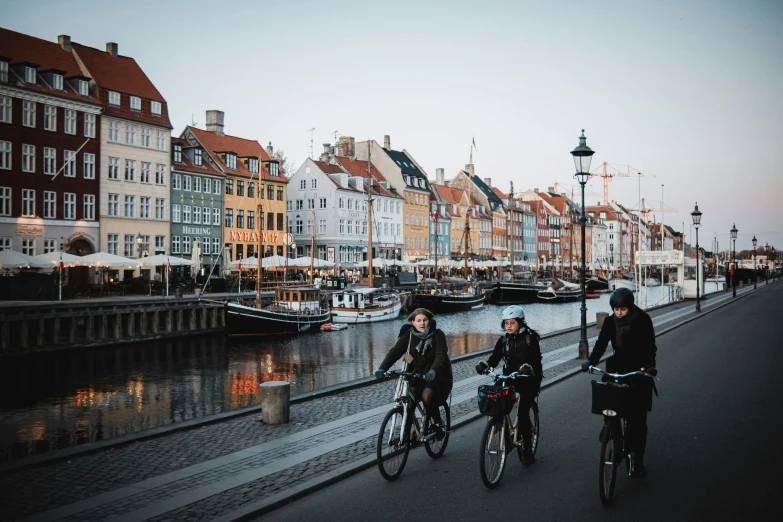 people ride bicycles down the road beside water in town