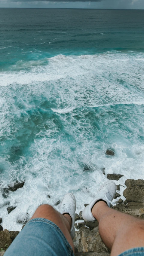 the feet of a man on a cliff above an ocean with strong waves