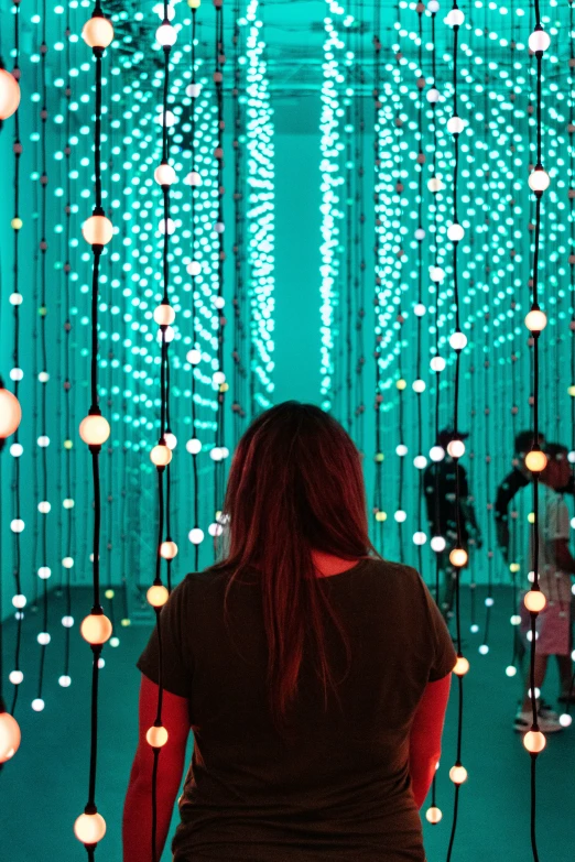 the view from behind a woman that is walking down a path through a building with lights on it