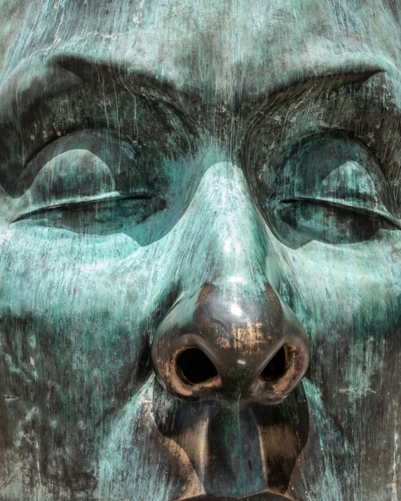 a bronze statue with eyes closed and a nose hanging from the center