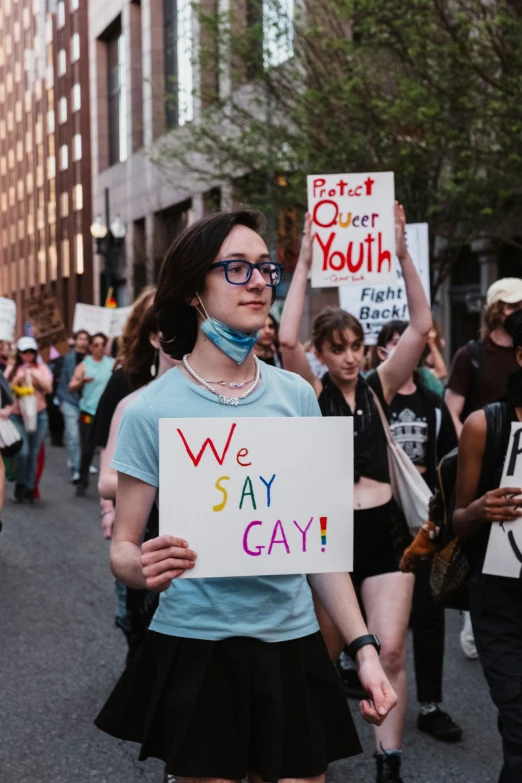 a woman wearing a face mask holds up a sign that says, we may 3 gay