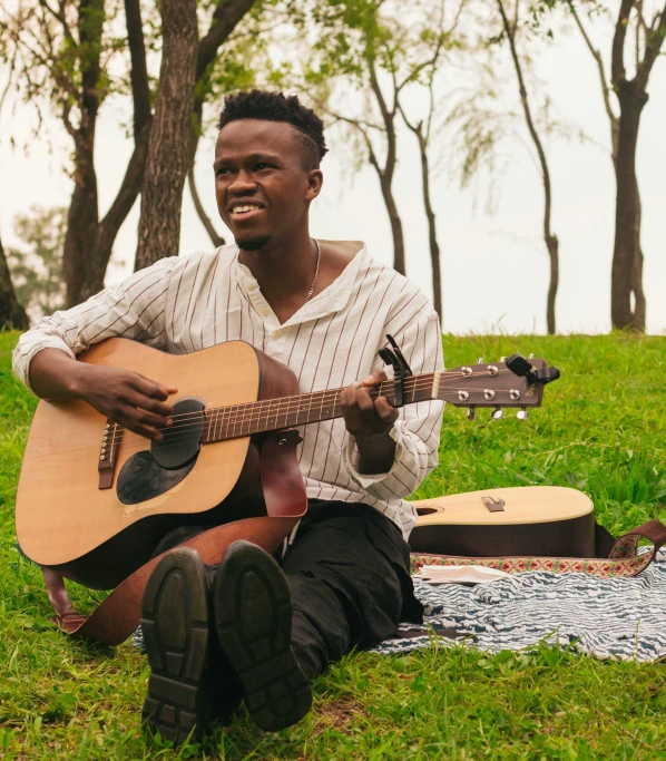 man sitting in the grass while playing guitar