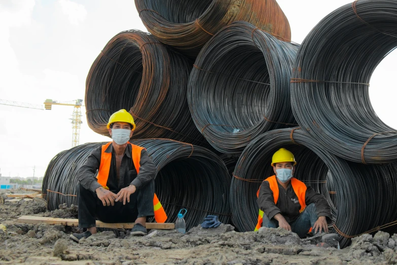 two men in yellow hardhats sit on some stacked steel wires