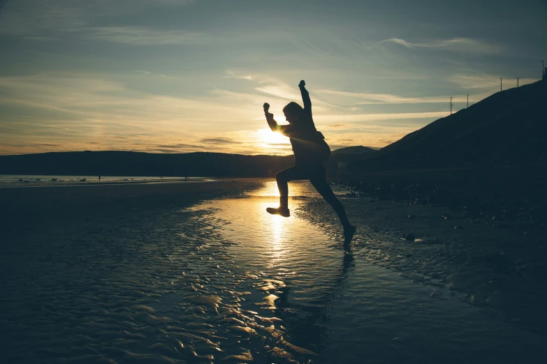 a man jumps into the air on the beach at sunrise