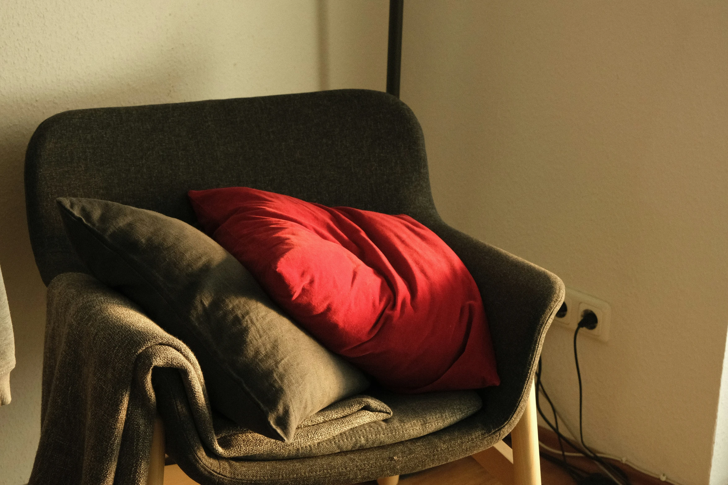a gray chair with pillows and a red pillow