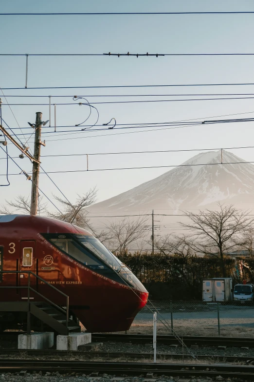 a red train passing under power lines and with snow on top