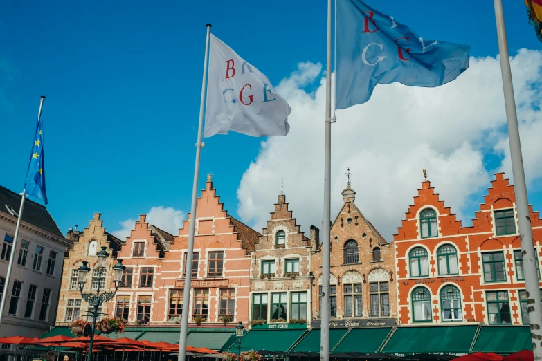 a row of flags flying in the sky with large buildings behind them