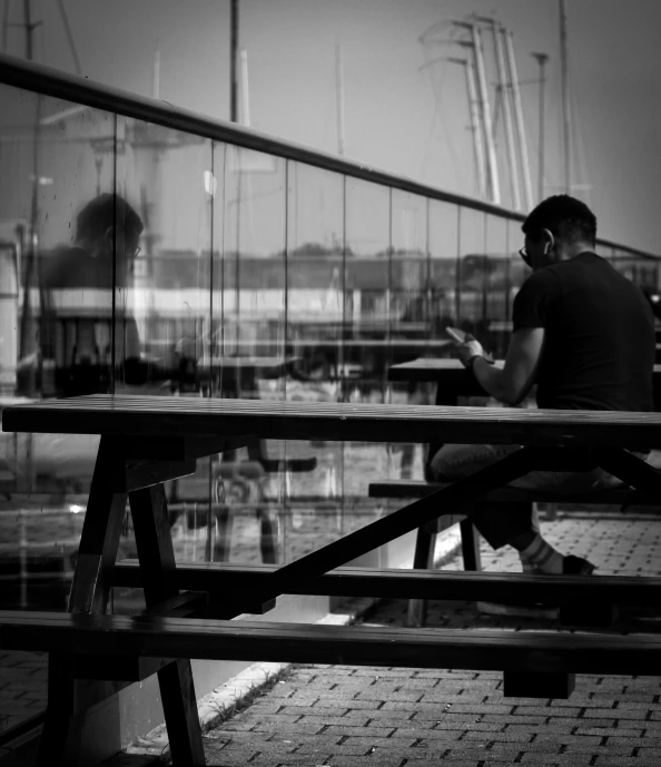 a man sitting on a bench at a boat dock with his phone