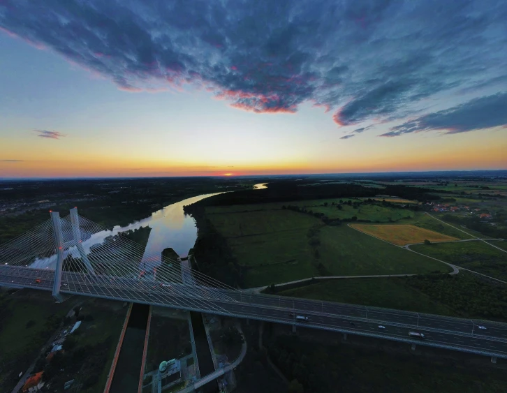 an overpass runs alongside a river as the sun sets