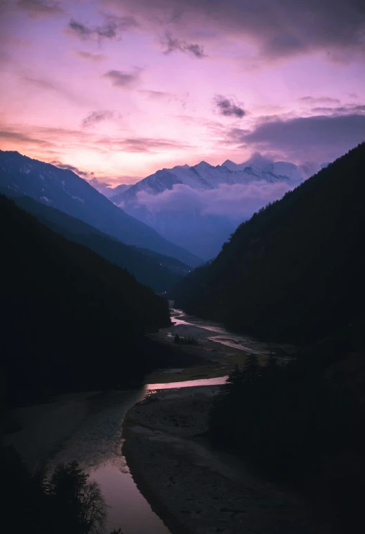 the sun sets on a river that is in the middle of mountains