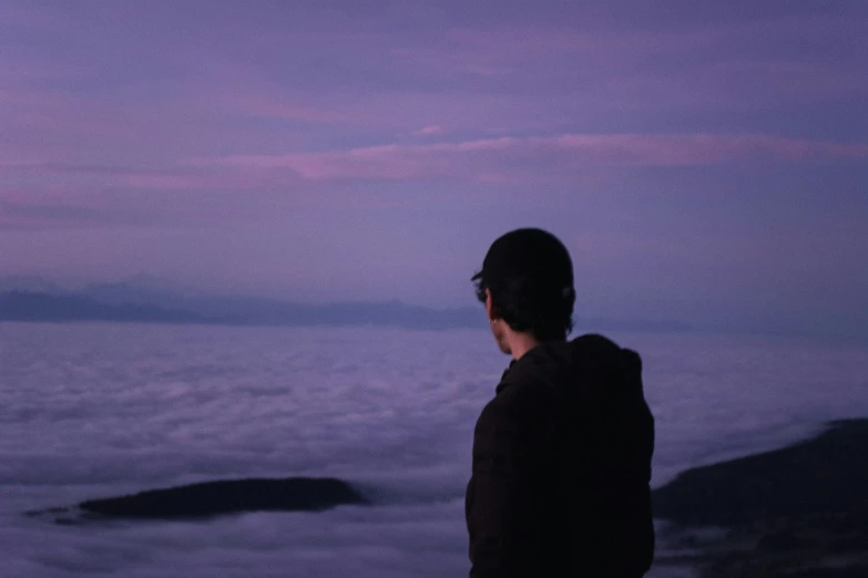 a man looking at the sea and a pink sky