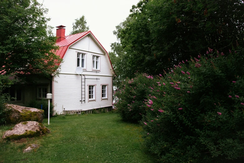 an old house on the grass with bushes and plants