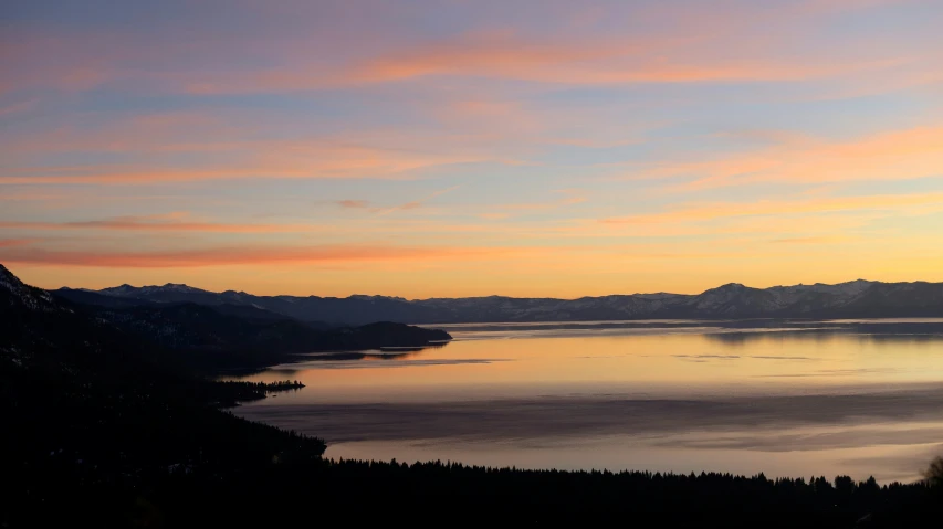 the sun sets over a lake and mountain range