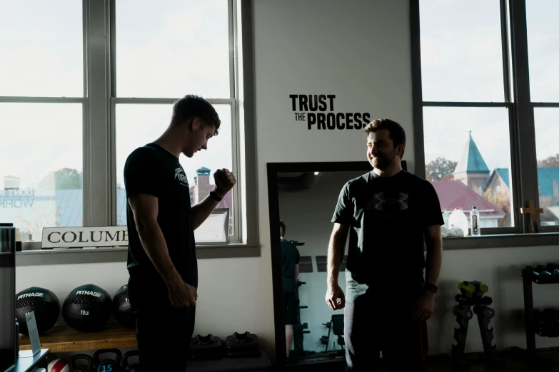 two men in the gym talking, both standing near a mirror