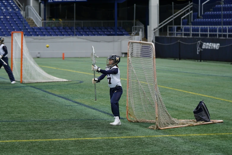 a girl holds her lacrosse stick while standing next to a goal