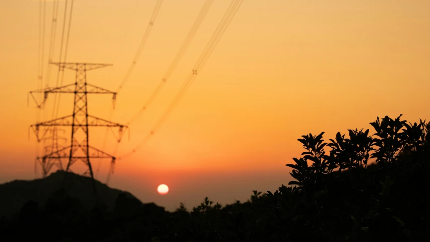 the sun rises in the distance behind a tall power pole