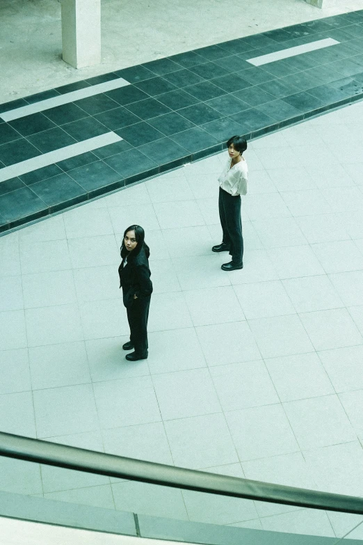 two people in black clothes stand in the middle of an empty parking lot