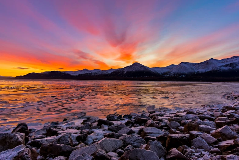 the sun setting over mountains next to a lake