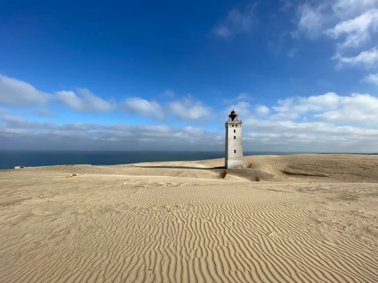 a very tall light house sitting on the edge of a sand dune