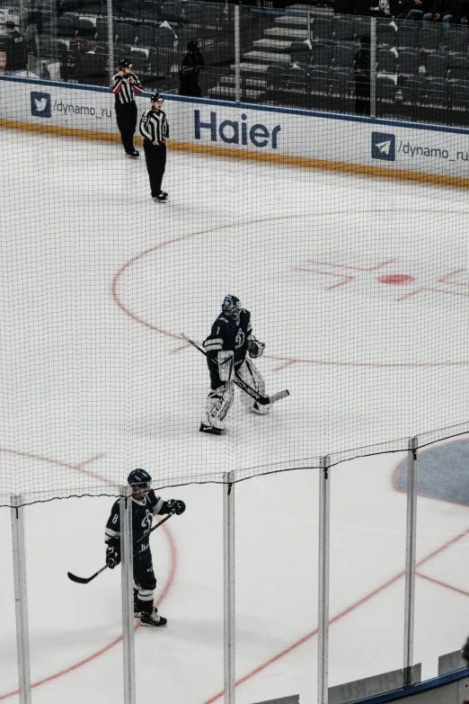 a goalie shoots a puck from behind the net as referee watches