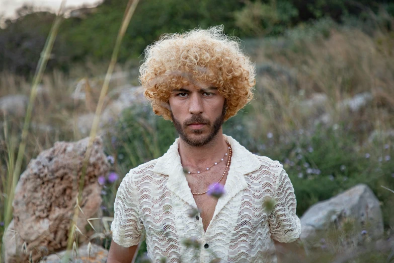 a man with very thick hair, wearing a white shirt and holding a flower necklace