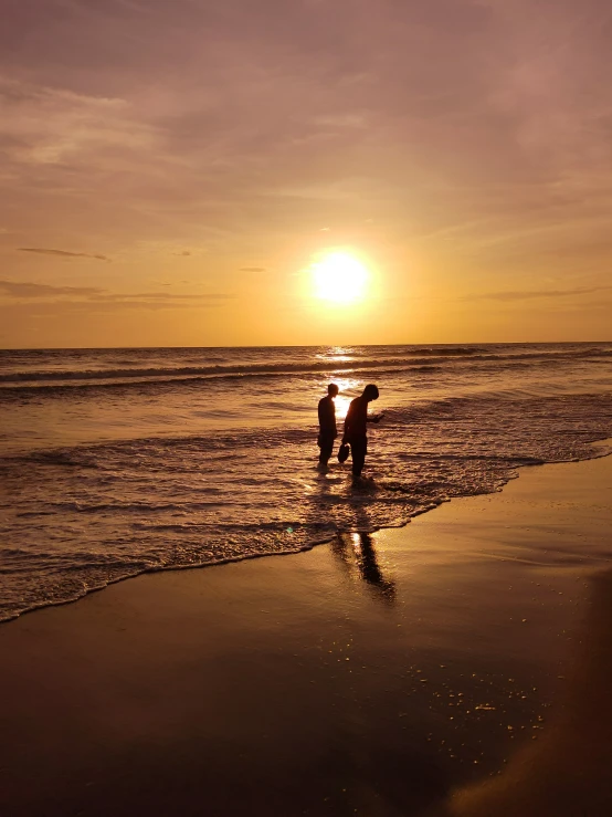 two people standing in the surf at sunset
