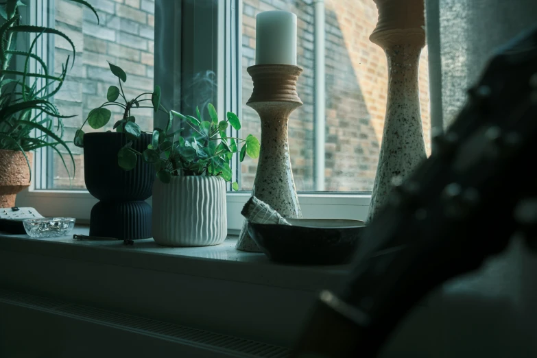 a white candle on a windowsill with various plant pots