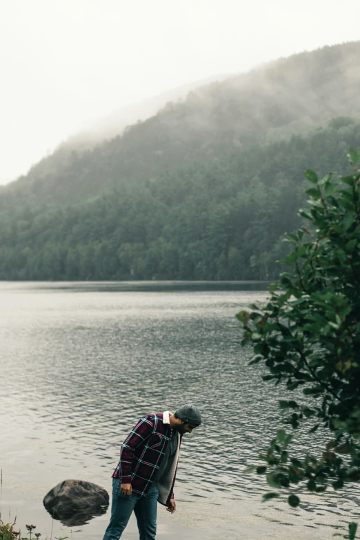 a man leans against the side of a body of water as rain drops over a mountainous area