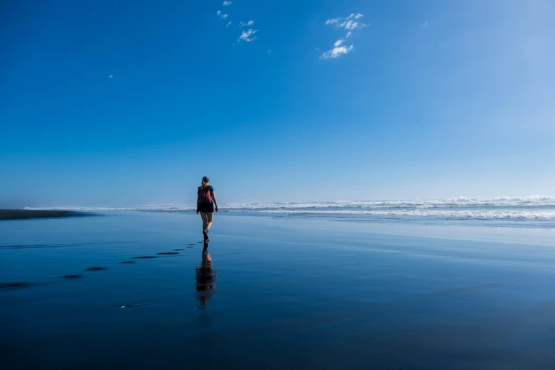 the lone person walks along a beach looking out at the ocean