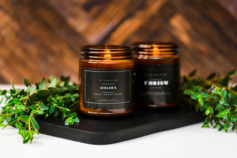 two brown candle jars with leaves on a black plate