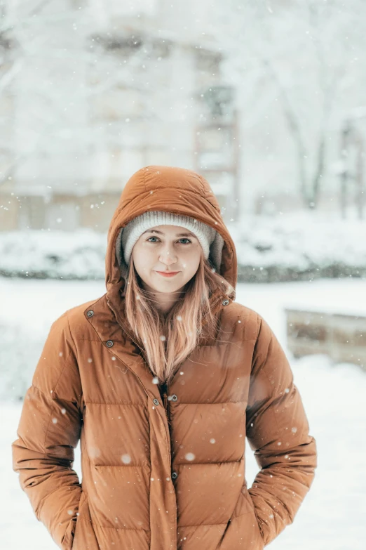 a woman stands in the snow wearing brown jacket and hat