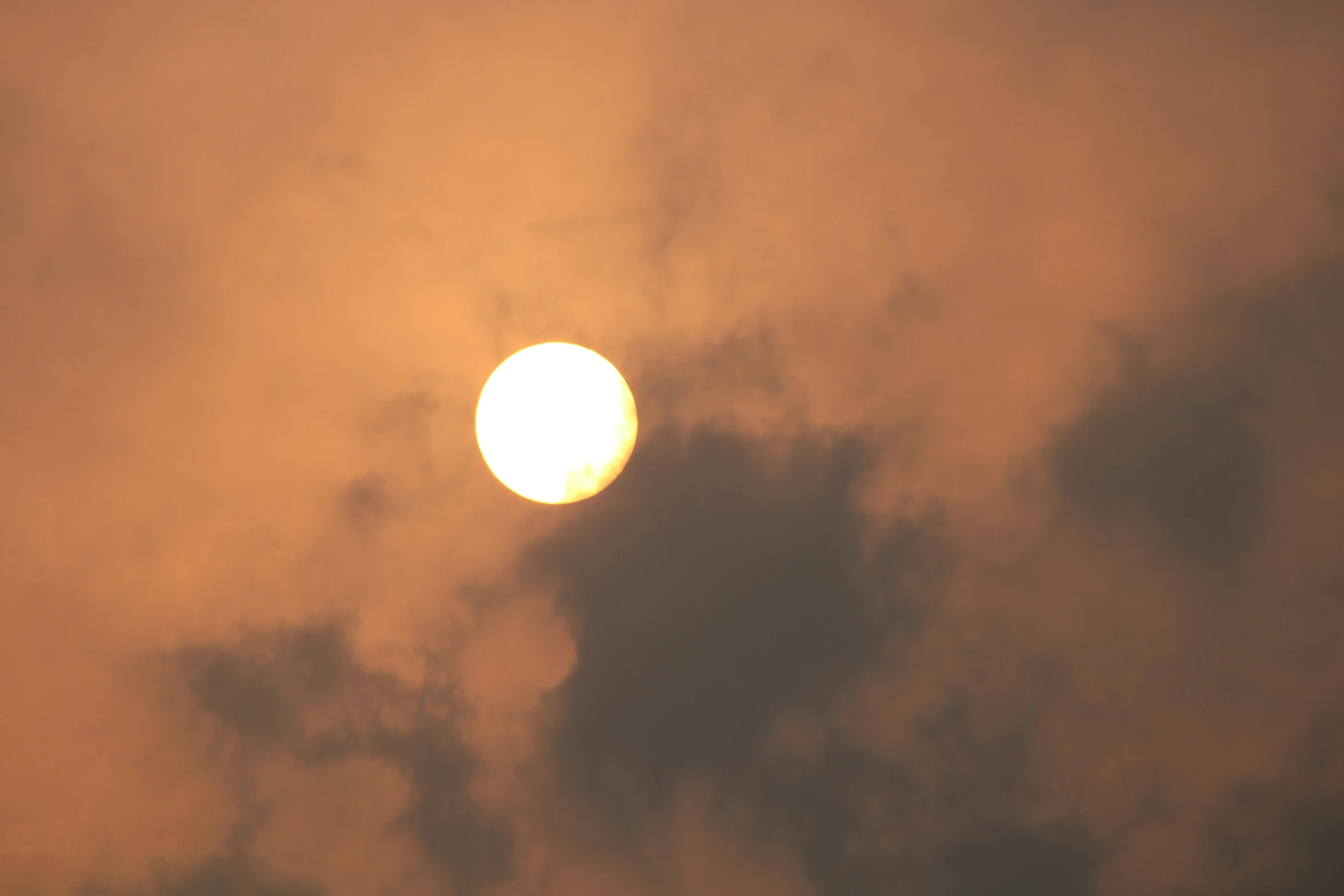 a yellow sun setting in the clouds on a partly cloudy day