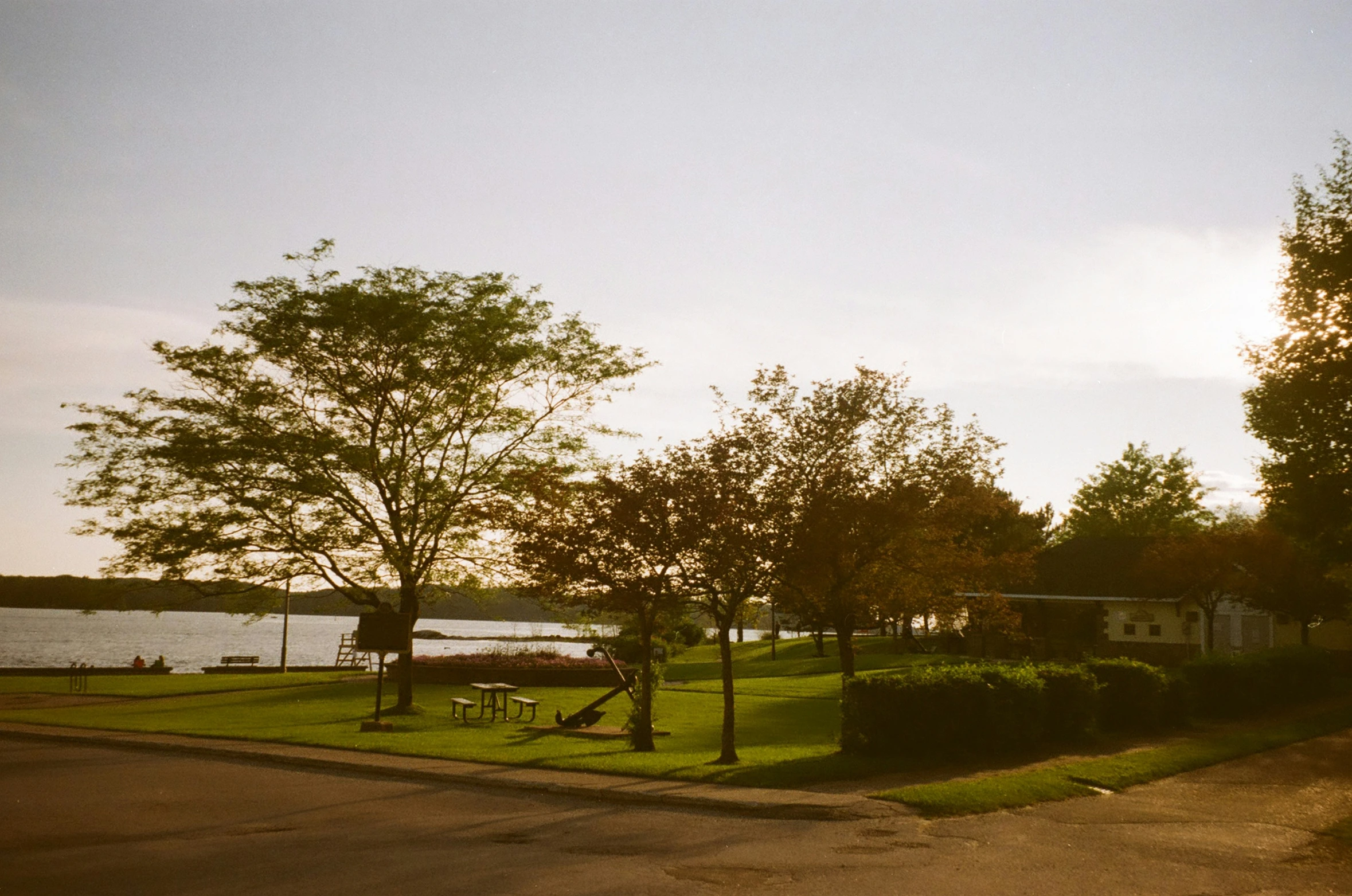 a park near the water at sunset, with grass and a house in the distance