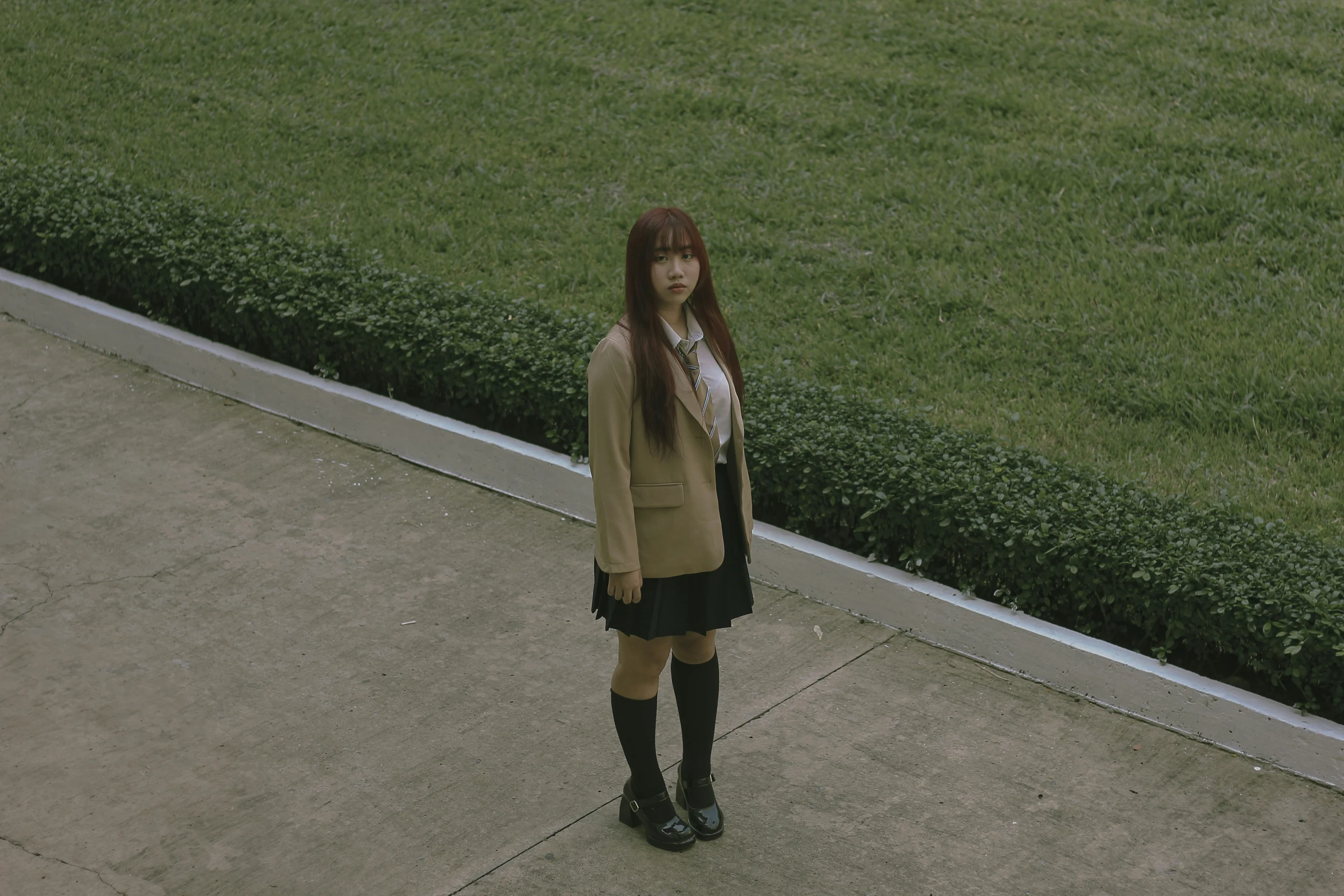 a woman standing on top of a sidewalk near green grass