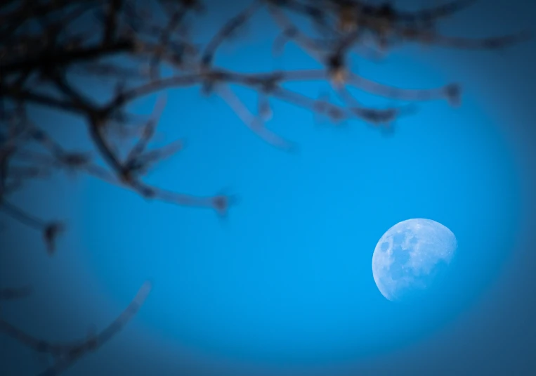 the moon is shining brightly against a blue sky