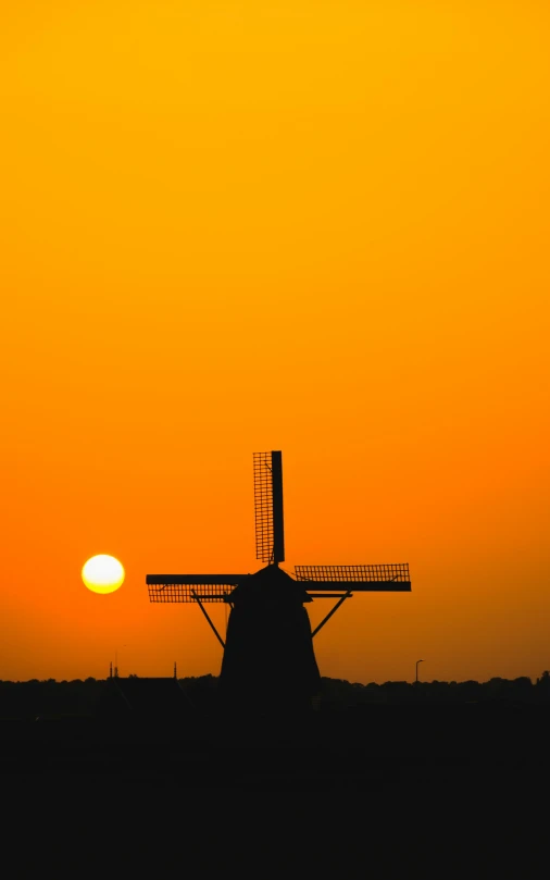 a windmill stands out against the bright yellow sky