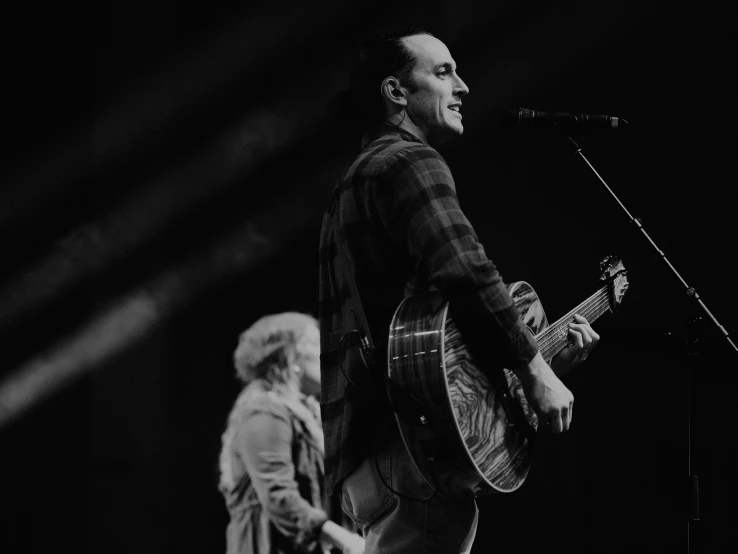 two people on stage one playing guitar and the other singing