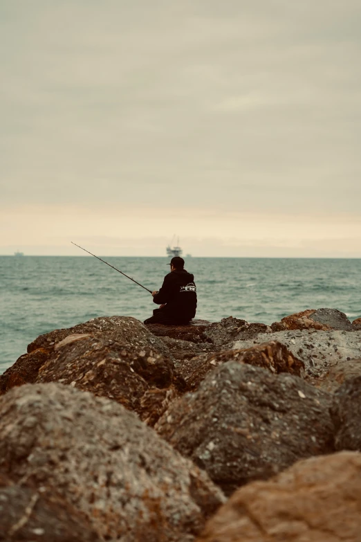 a man is sitting on some rocks fishing