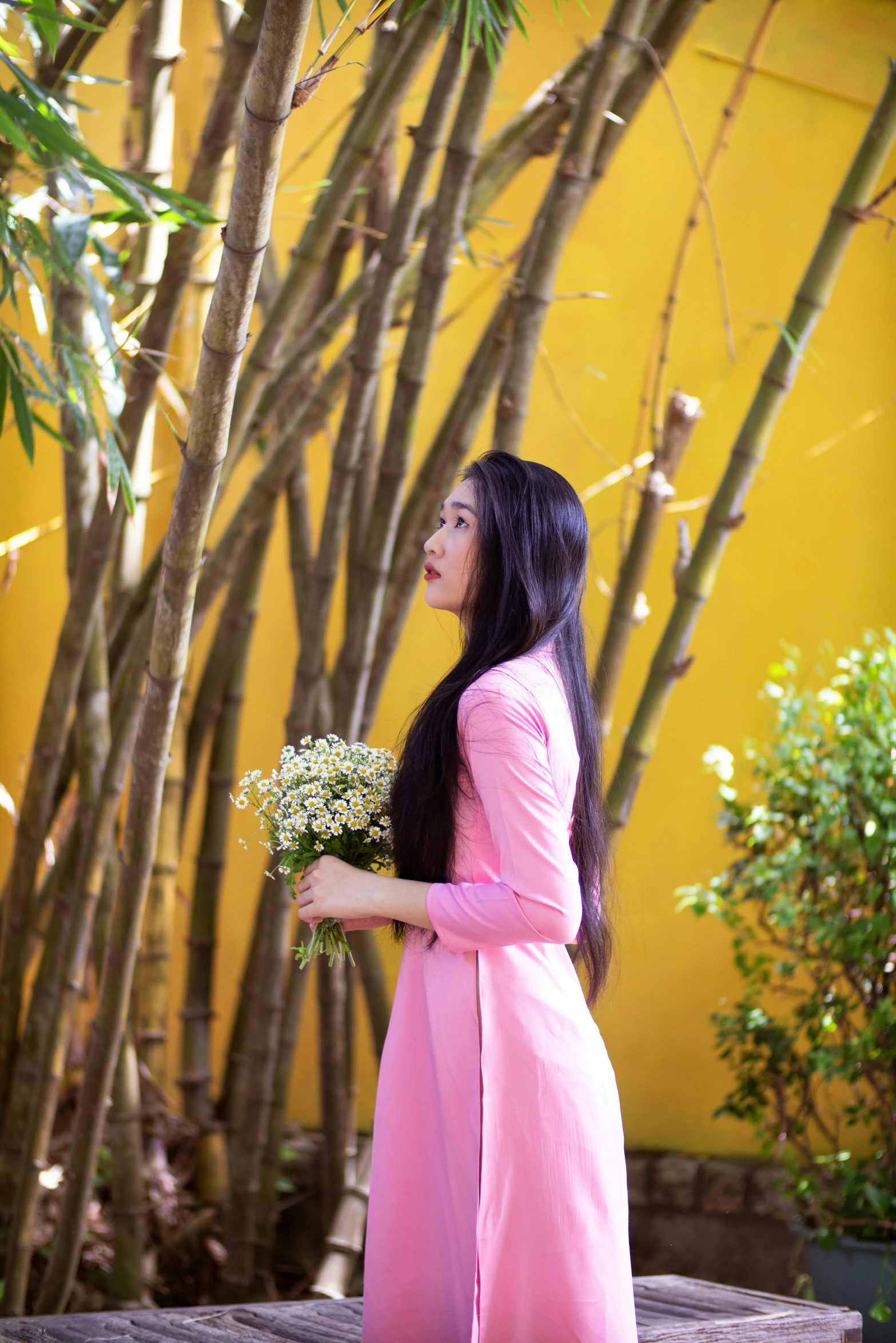 a woman standing in front of trees holding flowers