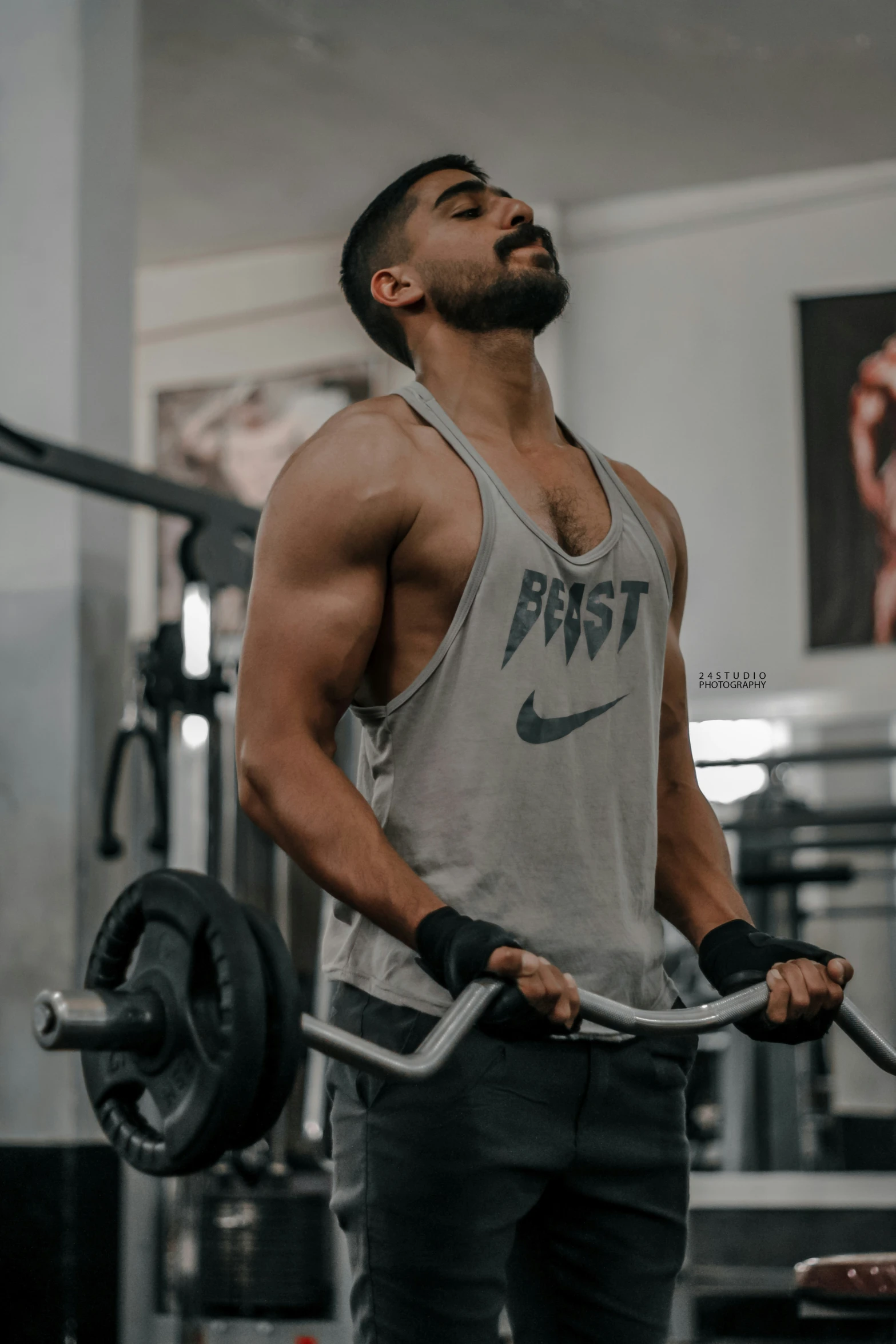 a man wearing gray tank top holding onto barbells in a gym