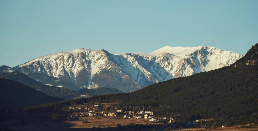 snow covered mountains in the distance with houses in a field below